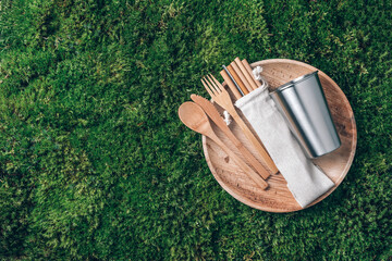 Sustainable lifestyle. Zero waste, plastic free, recycling concept. Stainless steel cup, wooden spoon, fork, knife, lunch plate and drinking bamboo straw on green grass, moss background