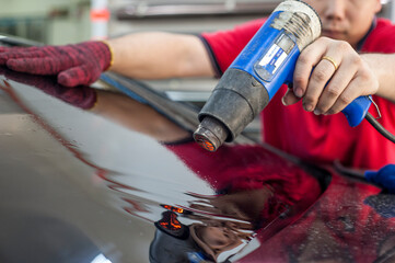 Car window tinting specialist attaching Tinting Film to car rear windscreen using Heat Gun.