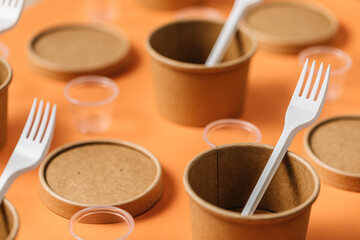 High angle of cardboard containers with plastic forks arranged with small plastic cups for takeaway food service on orange table