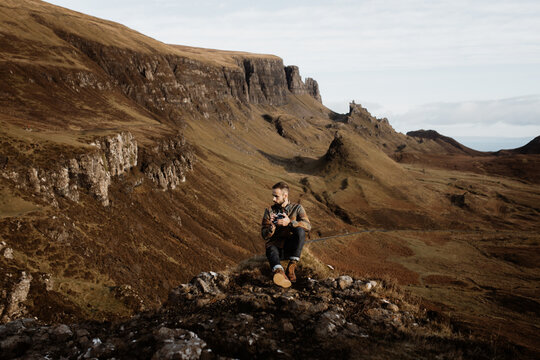 Male tourist with professional photo camera taking pictures and admiring wonderful mountains in Scottish Highlands in fall