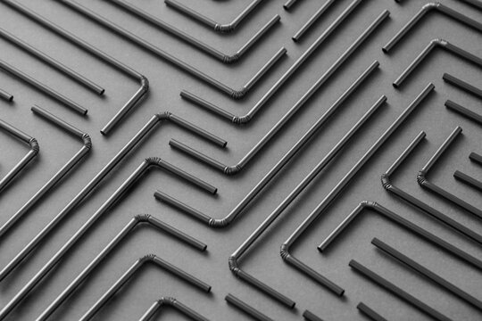 Top view flat lay composition with black plastic straws for takeaway drinks arranged in geometric ornament on black background