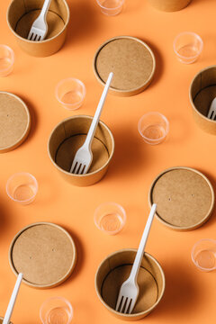 High angle of cardboard containers with plastic forks arranged with small plastic cups for takeaway food service on orange table