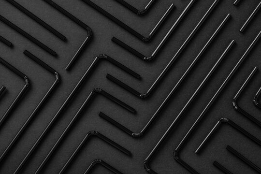 Top view flat lay composition with black plastic straws for takeaway drinks arranged in geometric ornament on black background