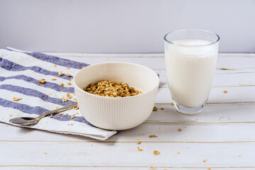 A bowl of cereal and a glass of milk on a wooden table with a towel. The concept of a healthy...