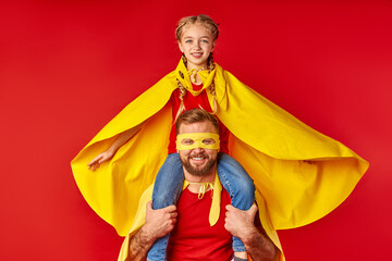 Obraz premium flying child girl on shoulders of super father isolated over red background, in yellow cloaks