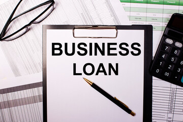 BUSINESS LOAN is written on a white sheet of paper, near the glasses and the calculator.