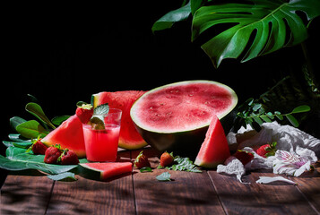 Glass of sweet fruit juice with mint arranged on wooden table with strawberries and ripe watermelon