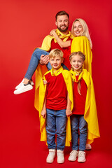 Fototapeta na wymiar family pretending to be superhero in the park, beautiful happy parents and children in superhero costume posing isolated over red background. entertainment concept