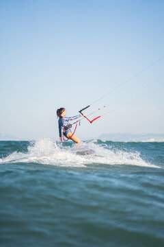 Side view of fit female kite surfer in swimsuit ridding waves in sea on sunny day in summer