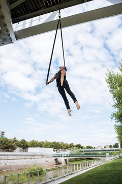 Low angle of fit male gymnast hanging on aerial straps during training in park