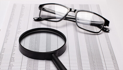 Black rimmed glasses and a magnifying glass lie on the reports