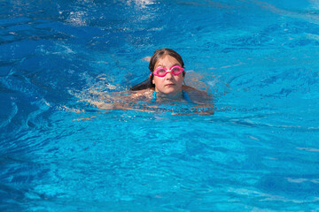 Girl in glasses swim in the blue swimming pool.