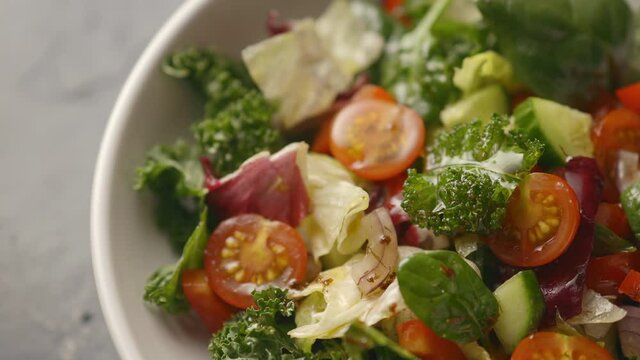 A juicy healthy vegetable salad is dressed with olive oil, the camera moves to the salad. Cucumbers, tomatoes, lettuce, iceberg lettuce. close-up