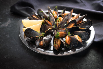 Mussels with lemon and parsley on a plate with a dark napkin on a black slate table, selected focus