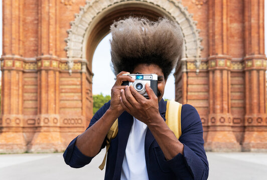Black man taking a picture while facing the camera with a camera in Arch of Triumph Barcelona