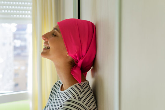 Young delighted female with cancer wearing headscarf standing in apartment