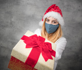 Santa woman giving christmas present box isolated on gray background. FOCUS ON FACE. Happy young girl holding gift. A Corona - Covid 19 Christmas concept