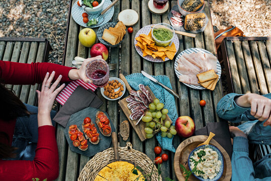 High angle of unrecognizable female friends sitting at wooden table in woods and eating tasty food during picnic in Valle del Jerte in summer