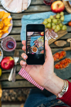 From above of anonymous crop female taking picture of table with various delicious food via smartphone during picnic in Valle del Jerte
