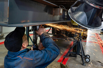 The welder works in the garage. Man working on a car trailer, A welder welds and assembles a truck trailer part in a garage. Service and repair of trucks - 393154903