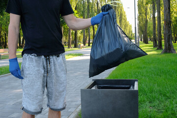 A male volunteer in the park puts plastic trash in a bag. Environmental problems, environmental...