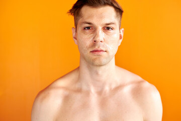 portrait of serious caucasian man with facial moisturizing cream on face, he confidently looks at camera, isolated over orange background
