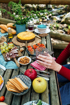 High angle of unrecognizable female friends sitting at wooden table in woods and eating tasty food during picnic in Valle del Jerte in summer