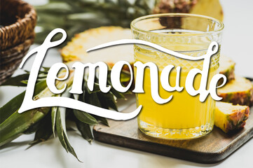 selective focus of fresh pineapple juice in glass near delicious fruit on cutting board and lemonade lettering on white