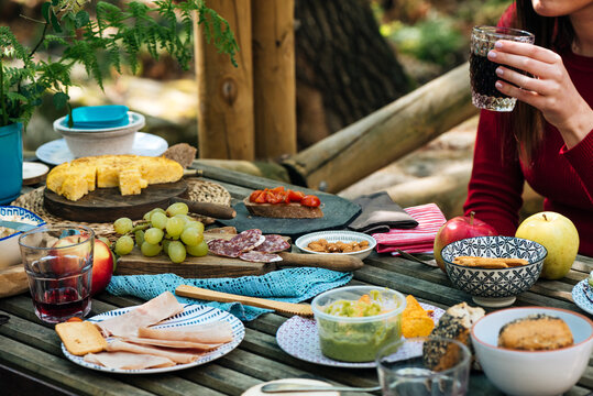 Unrecognizable female friends sitting at wooden table in woods and eating tasty food during picnic in Valle del Jerte in summer