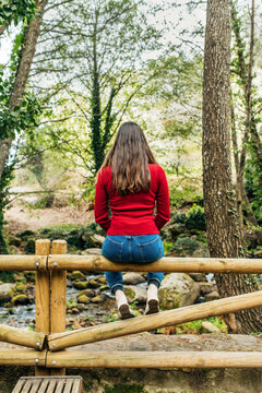 Back view of anonymous female tourist sitting on old bench in woods and admiring magnificent nature in Valle del Jerte