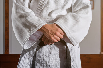 Cropped unrecognizable person standing with the arms crossed in a kimono with a black belt tied around his waist. Martial arts concept