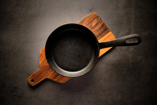 Top view of metal frying pan placed on wooden cutting board on table in kitchen