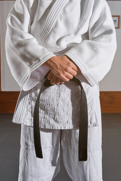 Cropped unrecognizable person standing with the arms crossed in a kimono with a black belt tied around his waist. Martial arts concept