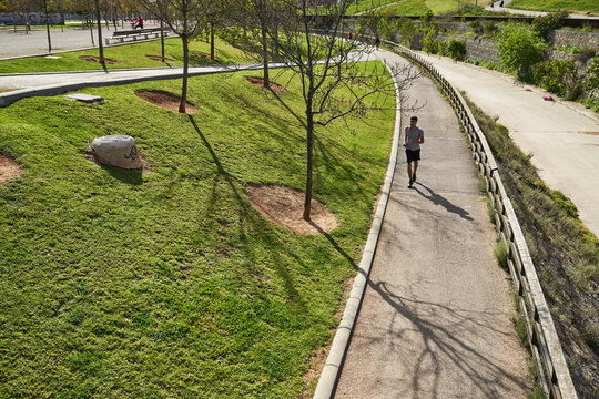 From above of sportive male in activewear running on paved path in park in sunny summer day