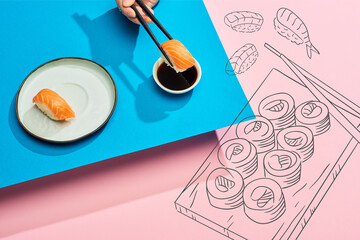 cropped view of woman putting fresh nigiri with salmon into soy sauce near japanese food illustration on blue, pink background