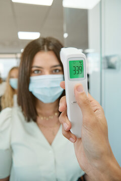 Receptionist with thermometer gun checking body temperature of coworkers before entering office space during coronavirus pandemic