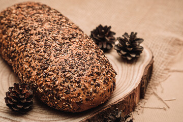 Rustic whole wheat bread with seeds on a wooden board with walnuts, pine cones and burlap fabric texture