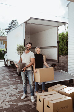 Portrait of smiling male and female partners unloading cardboard boxes during relocation