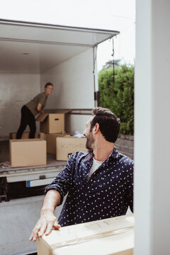 Smiling male looking at female friend while unloading cardboard boxes outside van