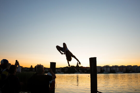 Man backflipping while friends photographing at lake during sunset