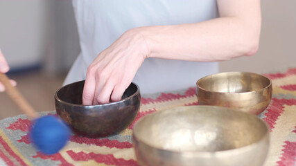 Woman playing on Tibetan singing bowl while sitting on yoga mat. Vintage tonned.