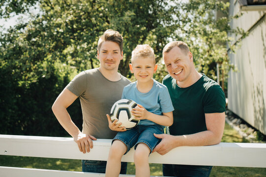Portrait of homosexual fathers with son holding soccer ball in yard