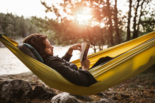 Contemplating man reading book while lying down over hammock in forest