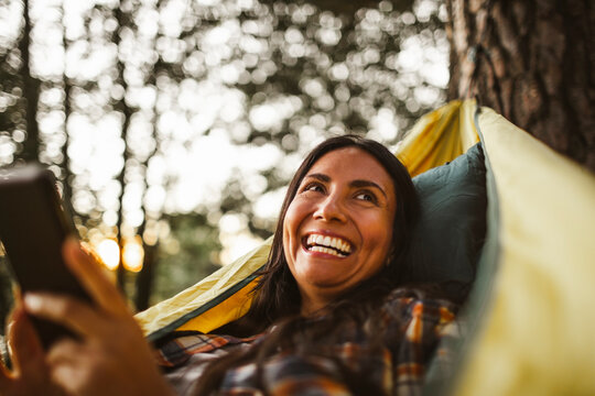 Woman using smart phone while lying over hammock in forest