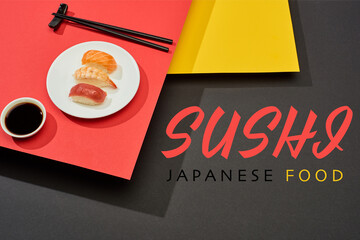 fresh nigiri with salmon, shrimp and tuna near soy sauce, chopsticks and sushi japanese food lettering on red, yellow and black surface