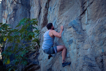 A young man with a rope engaged in the sports of rock climbing on the rock