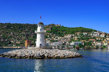 Fototapeta na wymiar Alanya deniz feneri close-up against the backdrop of the peninsula with the Red Tower and a fortress on the top of the hill. Seascape and cityscape of a modern Turkish tourist town among green nature
