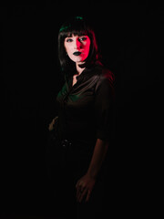 Girl with black makeup and black hair posing on a black background with colored light.