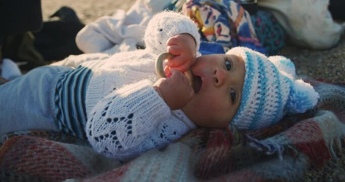 A little baby is lying on the beach in autumn and is chewing on a wooden teething ring
