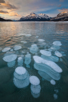 Sunrise over Elliot Peak and frozen bubbles in Abraham Lake in Alberta, Canada